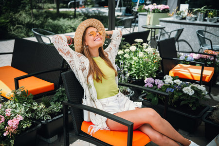 Relaxed sunny vacation mood woman in sunhat lounging at outdoor cafe garden enjoying summer fashion and lifestyle on a bright dayの写真素材