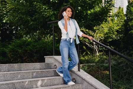 Young woman on a sunny outdoor commute walking down stairs while talking on a smartphone amid lush greeneryの写真素材