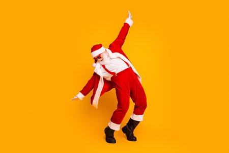 Santa Claus in a lively red suit strikes a dynamic pose against orange background for Christmas themed visuals and festive mediaの写真素材