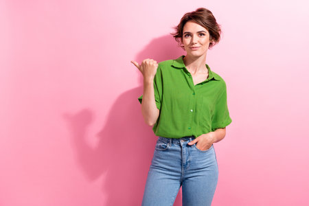 Photo of adorable pretty young woman dressed green shirt pointing thumb empty space isolated pink color backgroundの写真素材