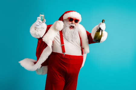 Santa Claus in red suit with a bottle and glass celebrates with friends and family against a bright blue background for a festive Christmas party moodの写真素材