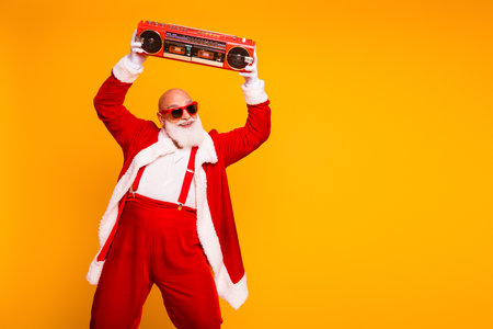 Santa in red costume with a boombox dances against a bright yellow background creating a playful festive Christmas party momentの写真素材