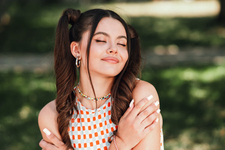 Young woman in a sunny park enjoying a relaxed moment in a bright checkered dress with ponytails and...