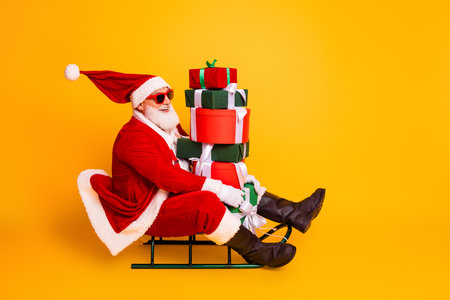 Santa on a sled carrying a stack of gifts wearing red costume hat beard and sunglass against a...