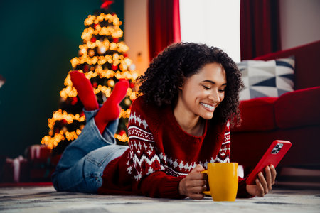 playful christmas moment at home woman on sofa with christmas tree lights phone and mug enjoying merry christmas vibesの写真素材