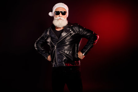 Cool Santa rocker in leather jacket and hat posing with hands on hips for holiday fashion and Christmas style photo shootの写真素材