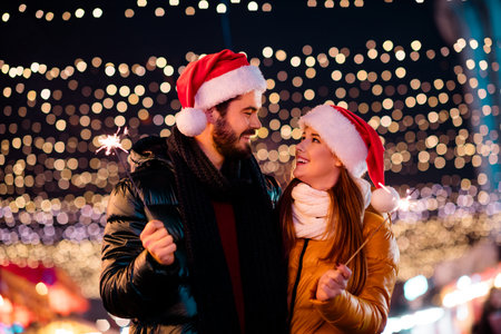 Whimsical Christmas night couple share joyous sparkler moments under magical market lights and cozy winter warmth togetherの写真素材