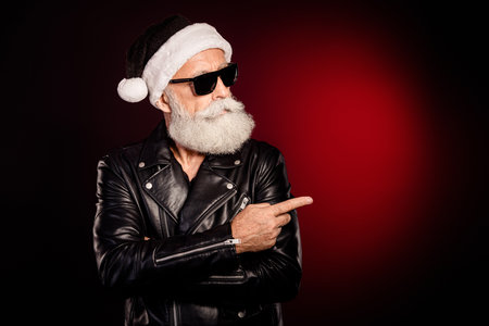 Rocking santa grandpa in leather jacket points to the right against a red illuminated backdropの写真素材