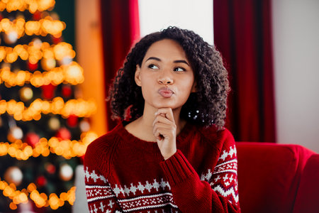 Playful woman in a red sweater by a twinkling Christmas tree in a cozy living room full of warm holiday glowの写真素材