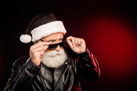Rocking Santa in a leather jacket and hat adjusts his sunglass for a bold festive look in a modern Christmas sceneの写真素材