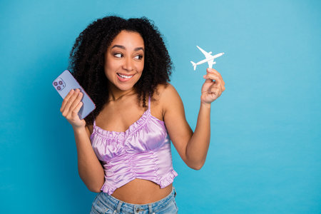Young woman with smartphone and toy plane exploring travel dreams in stylish casual fashion shoot