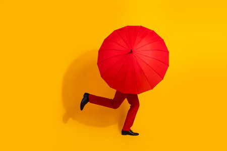 Dashing man in red suit runs with bright umbrella across a sunny yellow backdrop creating a bold playful imageの写真素材
