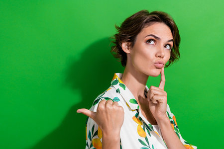 Photo of minded adorable girl wear trendy clothes arm touch face look up empty space offer banner isolated on green color backgroundの写真素材