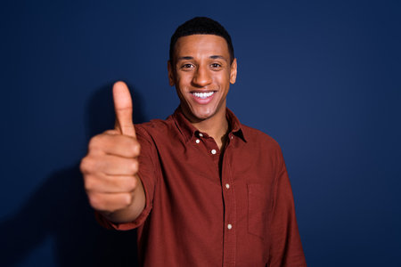 Photo portrait of nice young man approve show thumb up wear trendy brown outfit isolated on dark...