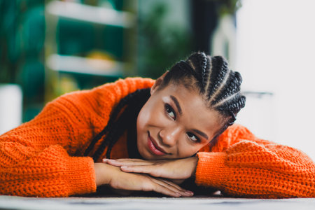 Young woman with braids rests on an orange knit sweater in a warm home interior feeling cozy and relaxed for lifestyle stock photoの写真素材