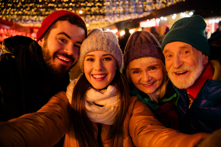 Joyful family friends and grandparents share a festive moment at a twinkling Christmas market outdoors under warm lightsの写真素材