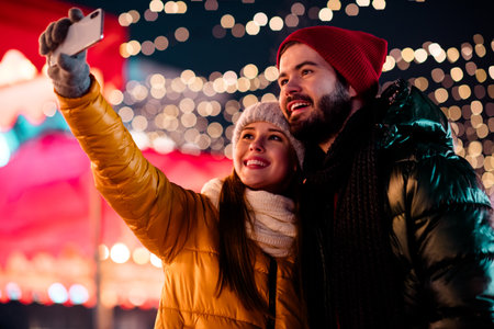 Funny couple selfie at festive market night with Christmas lights and snowy coats capturing love and joy for holiday season celebrationの写真素材