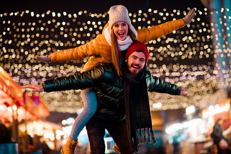 Delighted couple and friend enjoy festive street lights at a winter market full of joy and holiday glowの写真素材