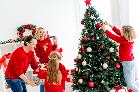 Family decorates a Christmas tree together indoors for a cozy home holiday sceneの写真素材