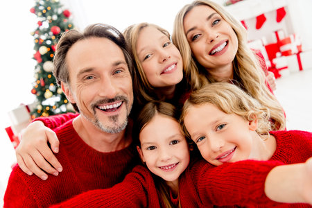 Joyful Christmas family moment at home with parents and children in red sweaters beside a decorated tree and giftsの写真素材