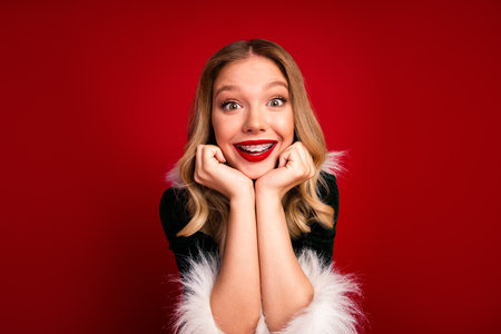 Joyful girl with red lipstick and braces smiles at the camera in a festive Christmas scene against a bold red backgroundの写真素材