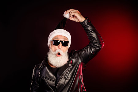 Rocking Santa in a black leather jacket with a white beard and sunglasses poses with hat for festive holiday stock photoの写真素材