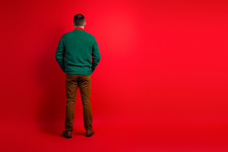 Funny man in green sweater stands against red backdrop ready for holiday mood and festive life style momentsの写真素材