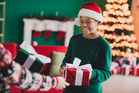 Festive young person exchanging Christmas gifts with joy in a cozy home decorated with a Christmas tree and lightsの写真素材
