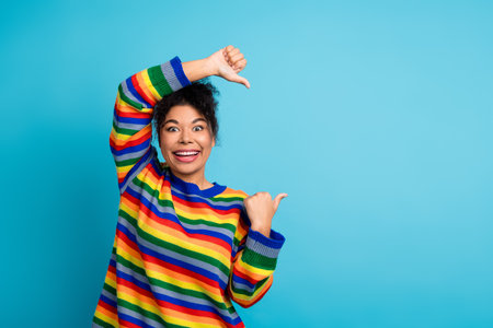 Joyful young woman in a colorful striped sweater poses against a blue background for fashion...