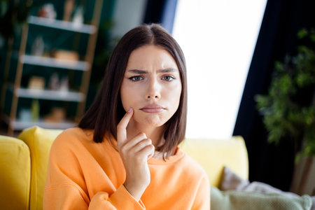 Curious young woman on a yellow couch in a bright living room thoughtful moment in home interior casual lifestyleの写真素材