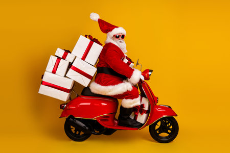 Santa on a red scooter delivering gifts in yellow studio creating festive holiday energy for Christmas shopping and seasonal promotionsの写真素材