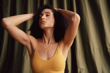 No filter photo of a young woman in a yellow top with her eyes closed, standing against a green curtain.の写真素材