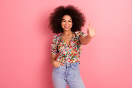 Portrait of a cheerful young woman with curly hair giving a thumbs up gesture in casual summer...