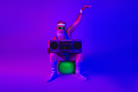 Elderly man in retro athlete outfit with boombox sits on a glowing ball under neon purple and blue lights for a disco fitness fashion vibeの写真素材