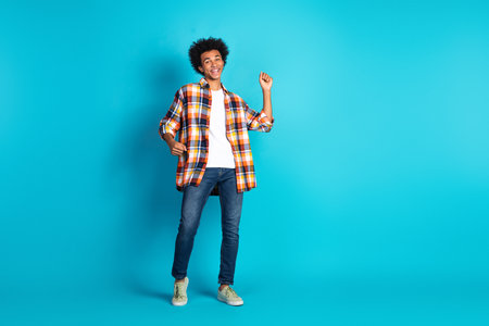 Young man in a colorful plaid shirt smiles and dances against a bright blue studio backdrop for a vibrant casual lifestyle and fashion stock photoの写真素材