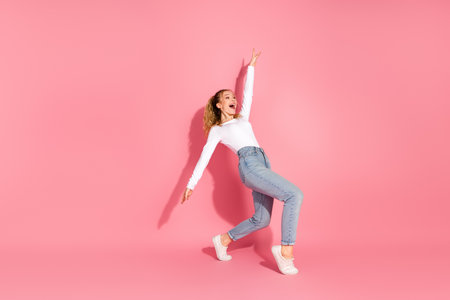 Young woman in casual style posing playfully against a pink background, showcasing trendy fashion and cheerful personality in studioの写真素材
