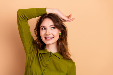 Young woman in green polo raises her arm with a cheerful smile against a warm beige background for lifestyle fashion advertisingの写真素材