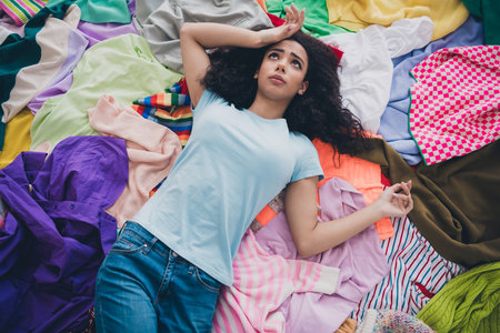 High angle view photo of young girl lay pile stack clutter clothes suffer head ache apartment indoorsの写真素材