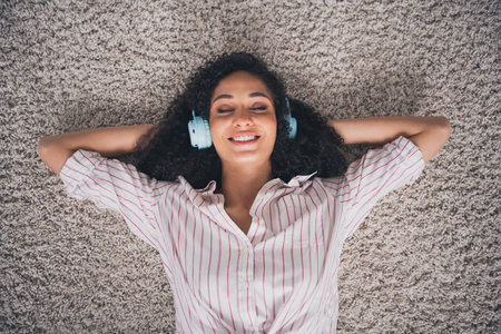 Top view photo of adorable sweet lady wear white shirt earphones arms behind head listening songs indoors room home houseの写真素材