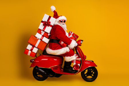 Santa on a red scooter loaded with gifts smiles in bright studio setting for Christmas adventure and holiday shopping vibeの写真素材