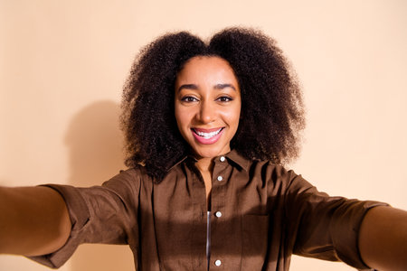 Photo of adorable toothy beaming girl with perming coiffure wear brown blouse make selfie smile isolated on pastel color backgroundの写真素材