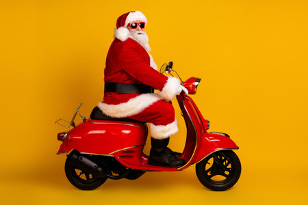 Santa on a bright red scooter wearing a costume with hat and beard in a vibrant studio setting for Christmas themed imageryの写真素材