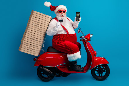 Santa on a red scooter fuels holiday magic as he carries pizza boxes and smiles for a festive photo in a bright blue studioの写真素材