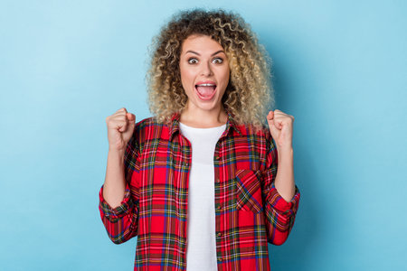Photo of funny celebrate glad victory raise fists wear checkered shirt isolated blue color backgroundの写真素材
