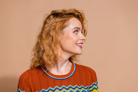 Portrait of adorable cheerful girl with ginger hairdo wear knit t-shirt look at proposition empty space isolated on beige color backgroundの写真素材