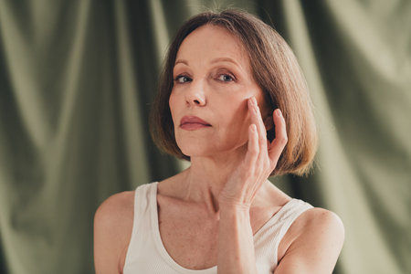 Unretouched photo of old lady look touch fingers facial skin isolated green color linen backgroundの写真素材