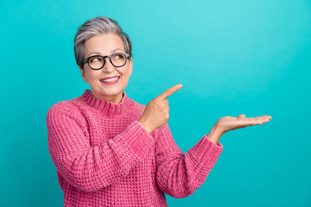 Portrait of smart woman wear pink pullover in glasses look directing at offer on palm empty space isolated on turquoise color backgroundの写真素材