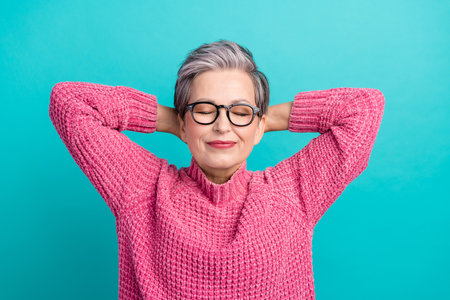 Portrait of sleepy woman with gray hairdo wear pink pullover hold palms behind head take nap isolated on turquoise color backgroundの写真素材