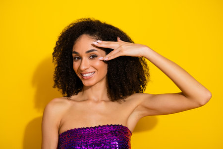 Beautiful young woman with curly hair showcasing glamour chic style in a bright yellow studioの写真素材