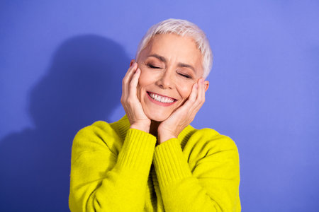 Smiling mature woman with short white hair in a bright yellow sweater enjoying happiness against a purple background for lifestyle wellnessの写真素材